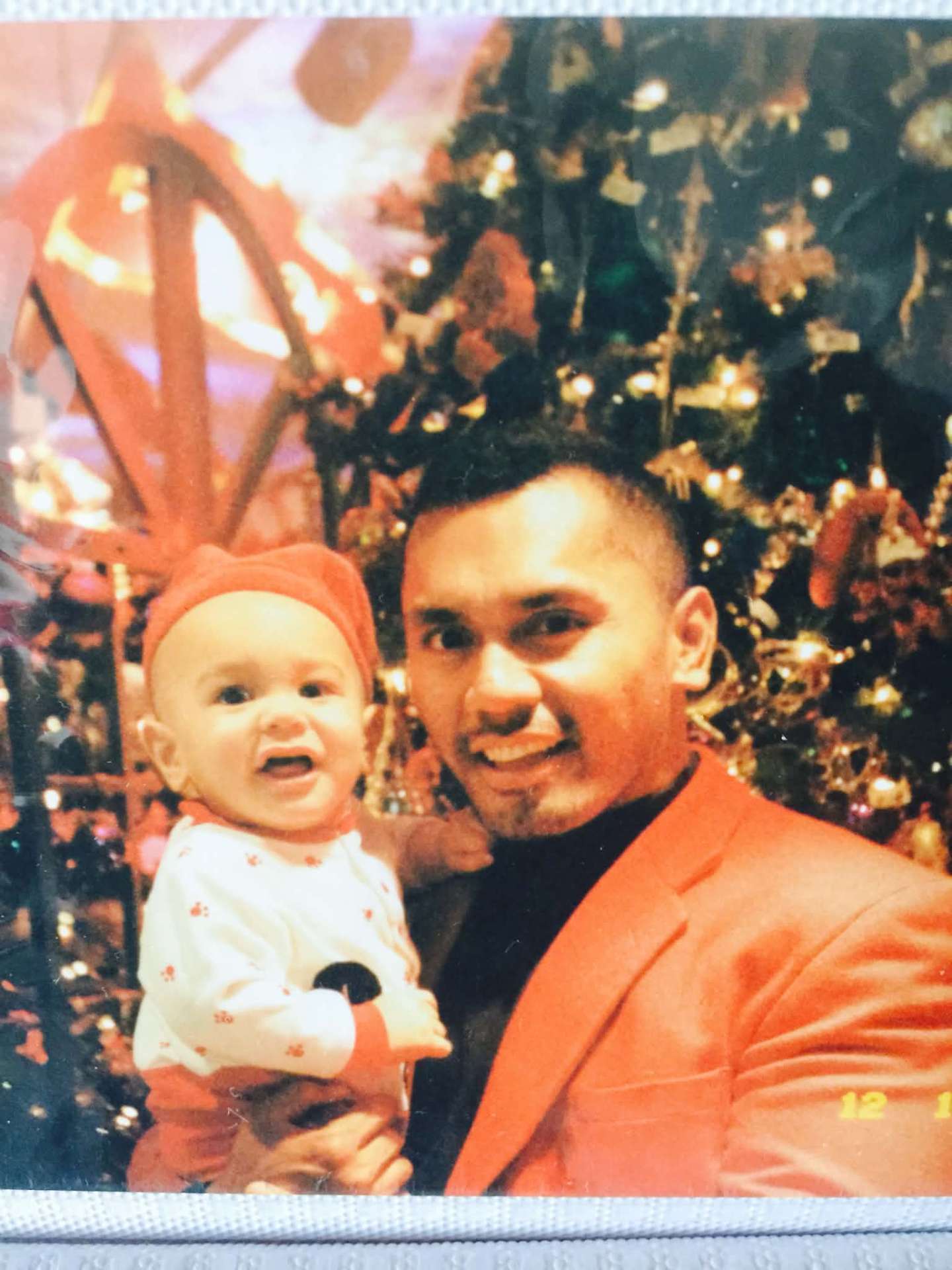 Dad in a red jacket holding a baby in front of a Christmas tree